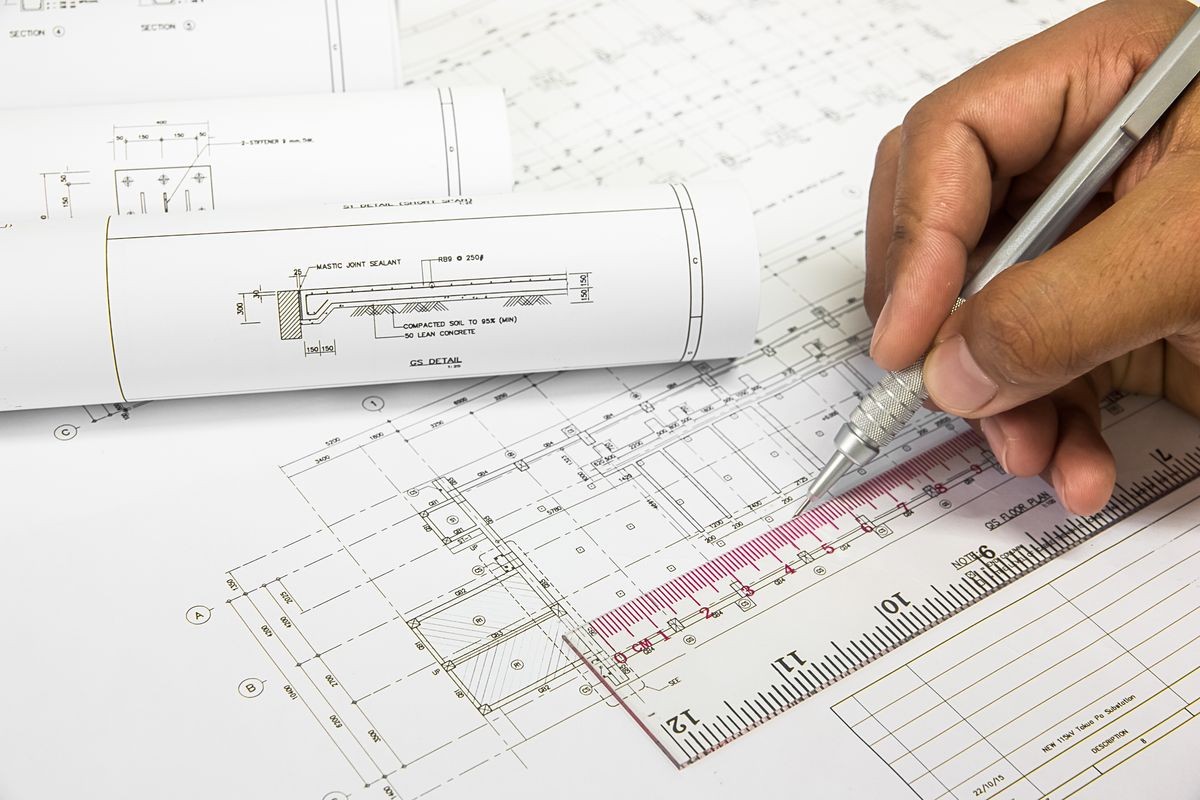 Hand holding a pencil, ruler engineer writing on the Blue Print a blueprint. Place the rolls on a desk over blurred blueprint.